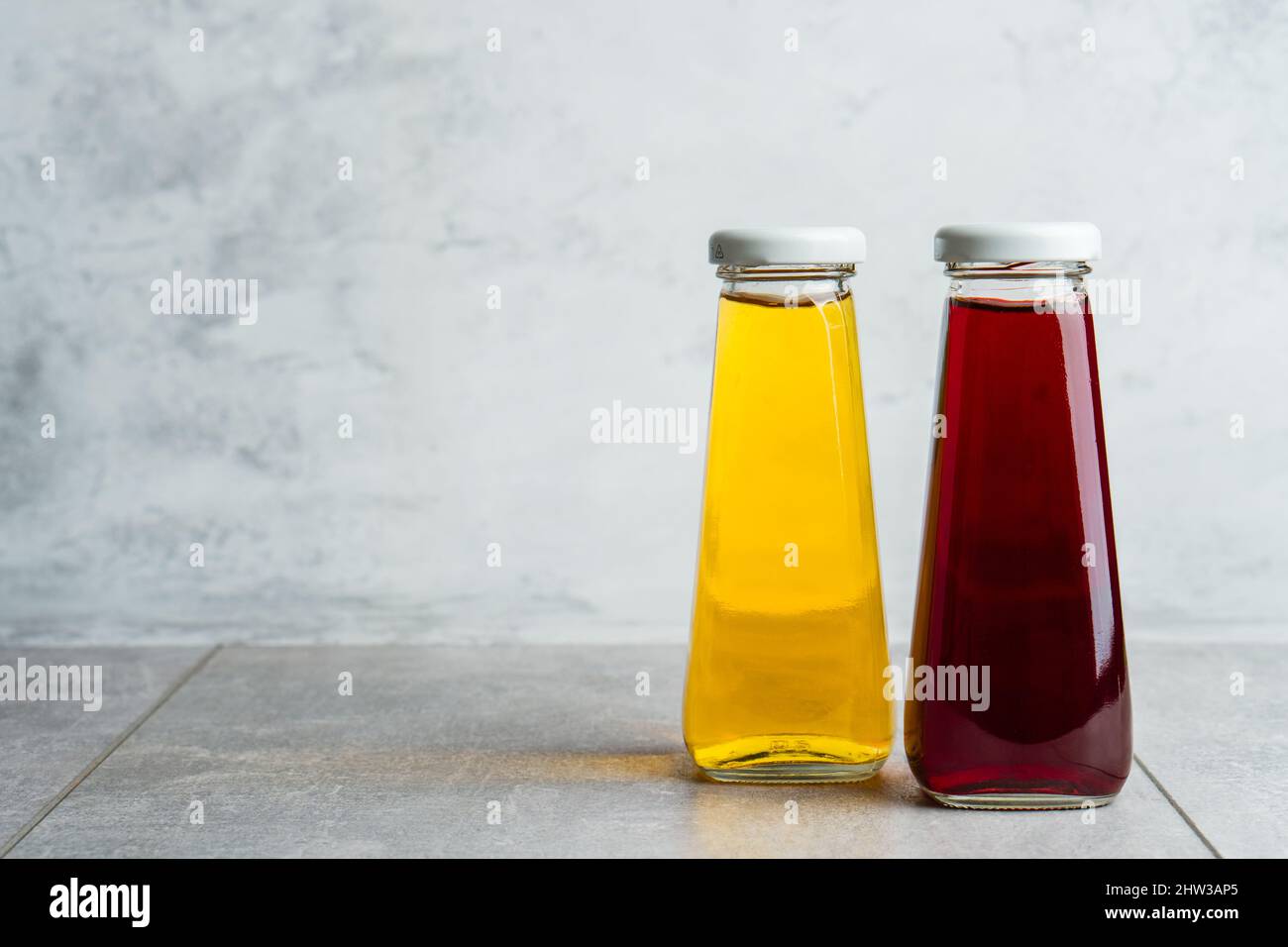 Bottiglie con bevanda a base di acqua halthy liquida gialla e rossa su sfondo grigio. Succo d'arancia e di ciliegia Foto Stock