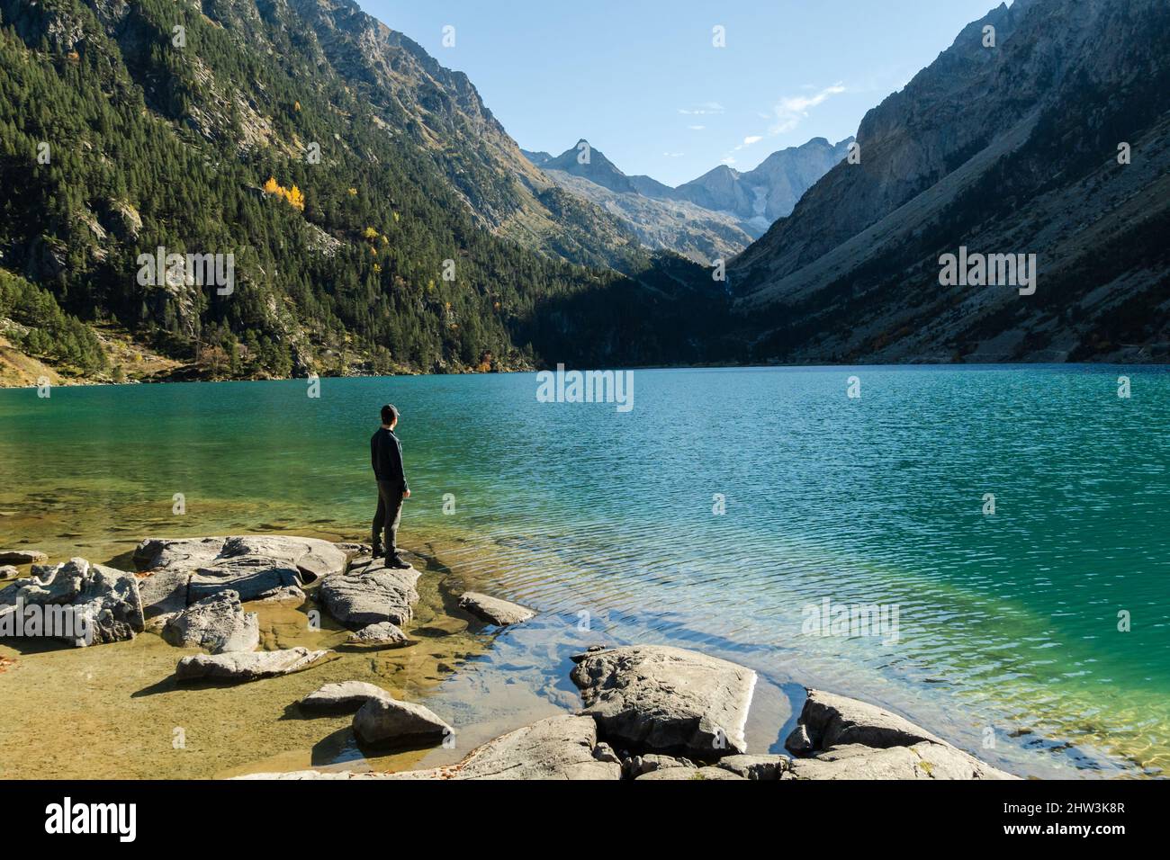 Il giovane viaggiatore fa scalini sulle rocce sulla riva del Lac de Gaube nei Pirenei francesi Foto Stock