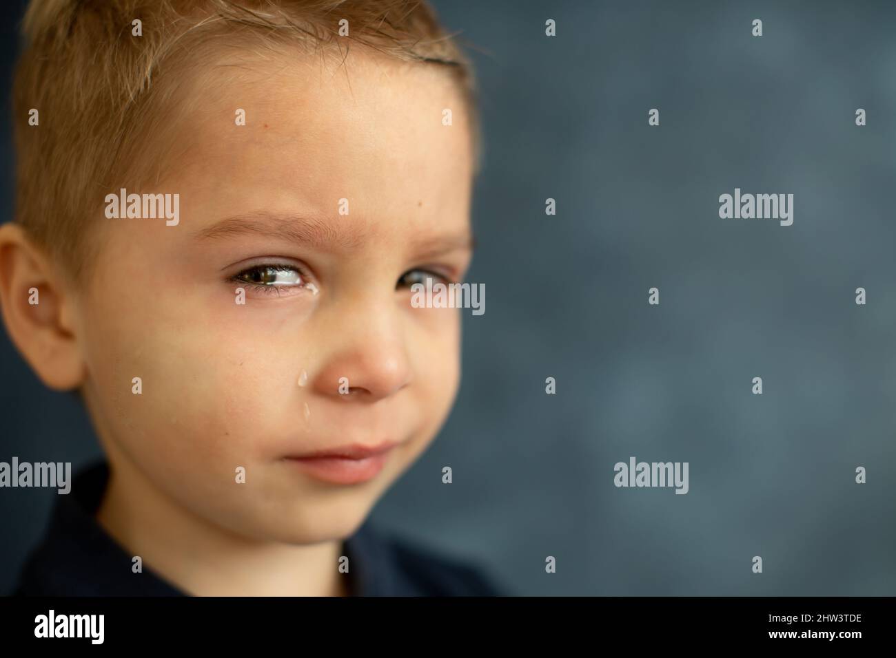 Bambino triste, ragazzo biondo, piangente, immagine isolata su sfondo blu Foto Stock