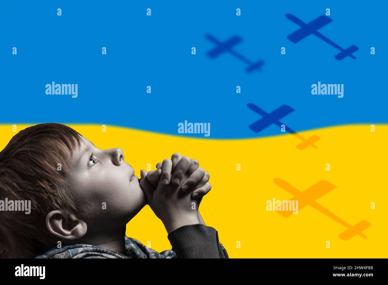 Un bambino prega sullo sfondo della bandiera Ucraina. Aggressione russa. Aerei volanti. Foto Stock