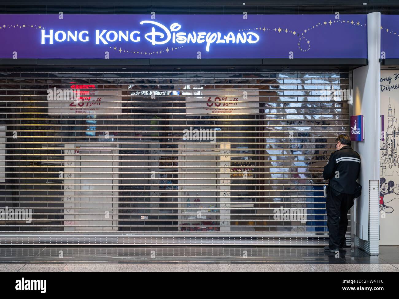 Hong Kong, Cina. 16th Feb 2022. Un uomo si erge di fronte ad un parco divertimenti a tema ufficiale Disney, il negozio Disneyland nell'aeroporto internazionale di Hong Kong, dato che la maggior parte degli affari sono chiusi a causa della diffusione della variante covid-19. Credit: SOPA Images Limited/Alamy Live News Foto Stock