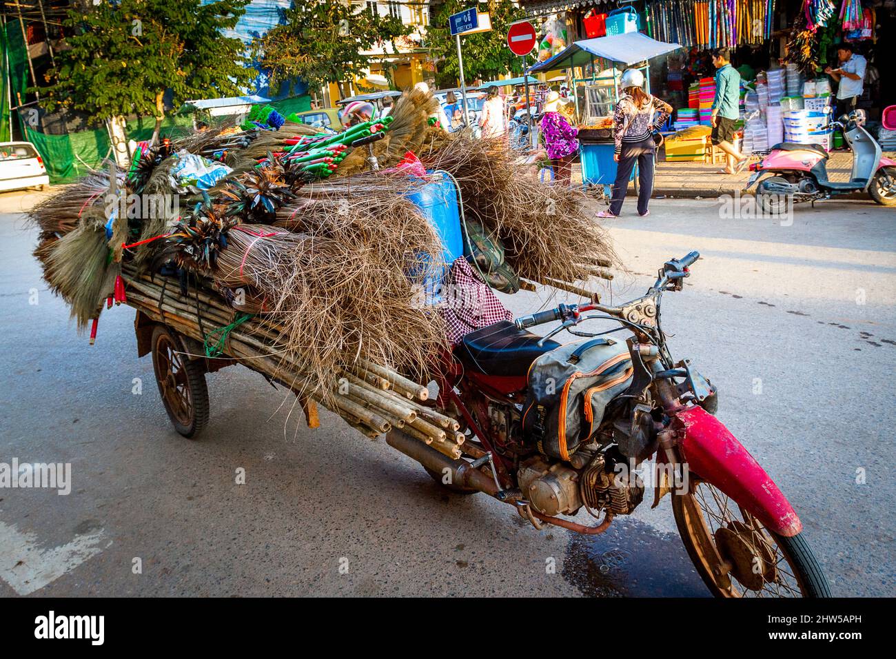Una moto rossa con un carro agganciato alla schiena che porta legno, bambù, scopa, per la consegna, è parcheggiata sulla strada di fronte al mercato Vecchio. Foto Stock