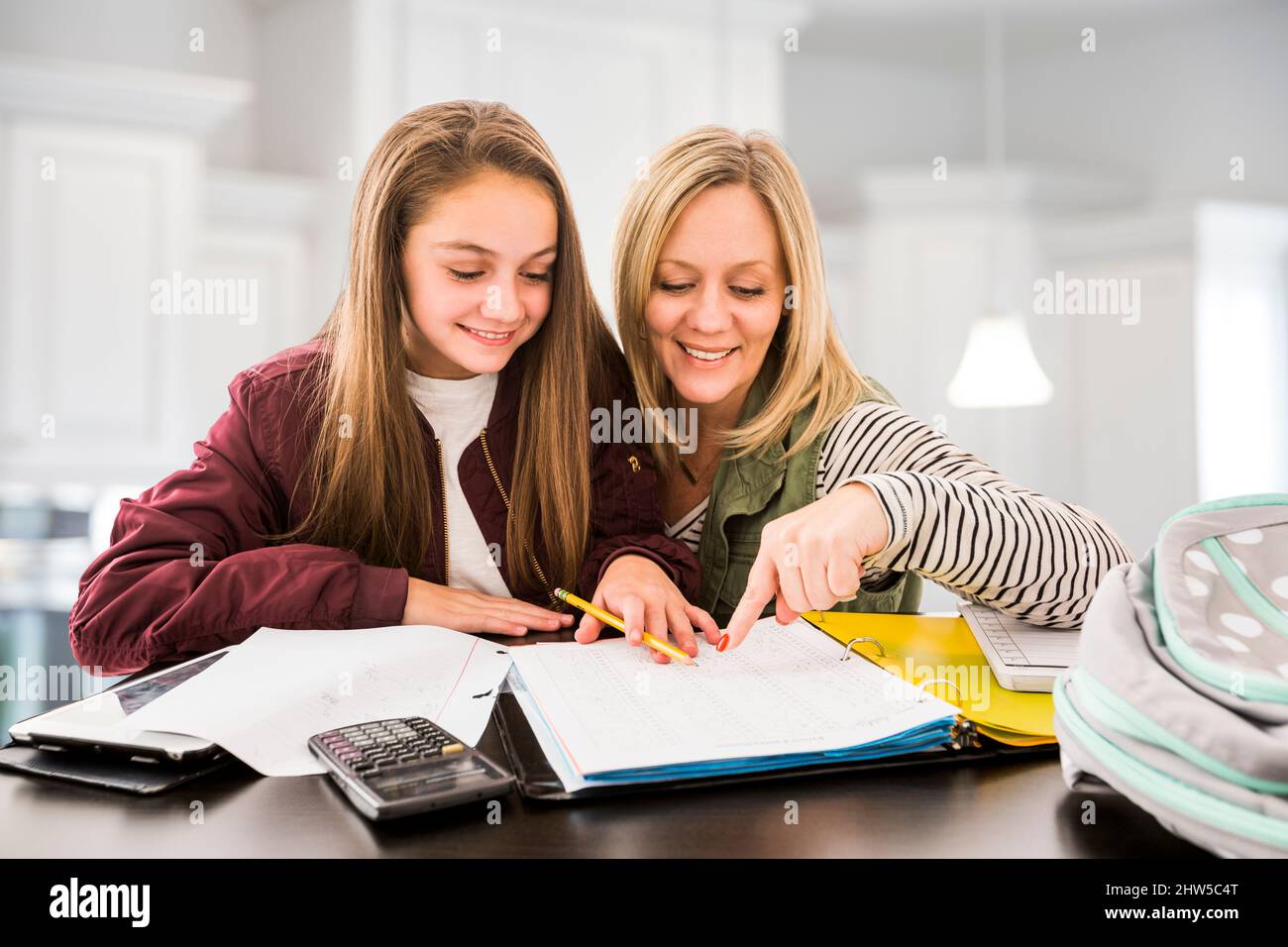 Madre che aiuta la figlia (12-13) che fa i compiti alla scrivania Foto Stock