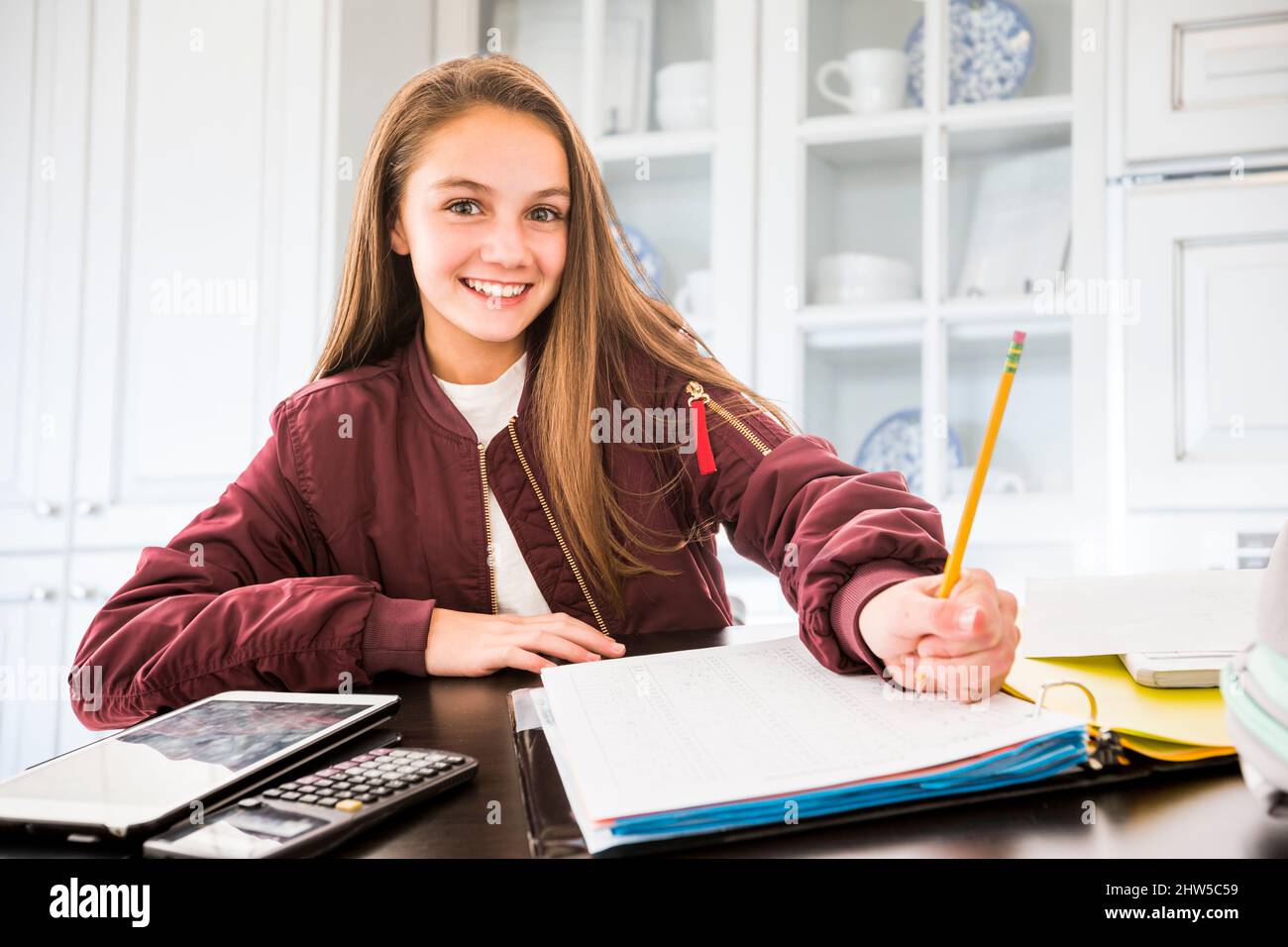 Ritratto della ragazza sorridente (12-13) che fa i compiti alla scrivania Foto Stock