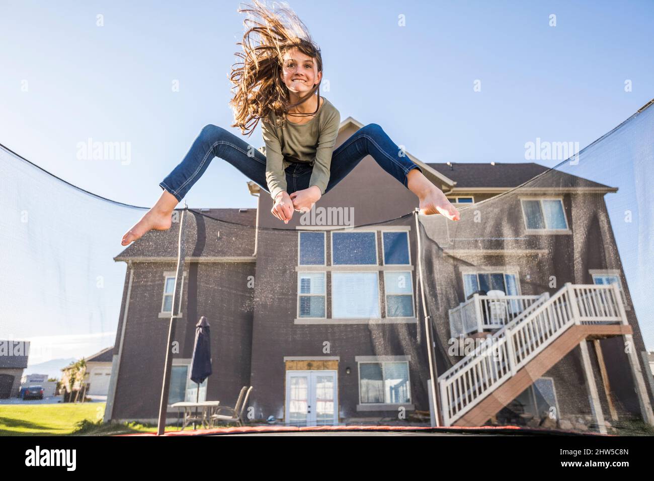 Ragazza (12-13) saltando sul trampolino di fronte a casa Foto Stock