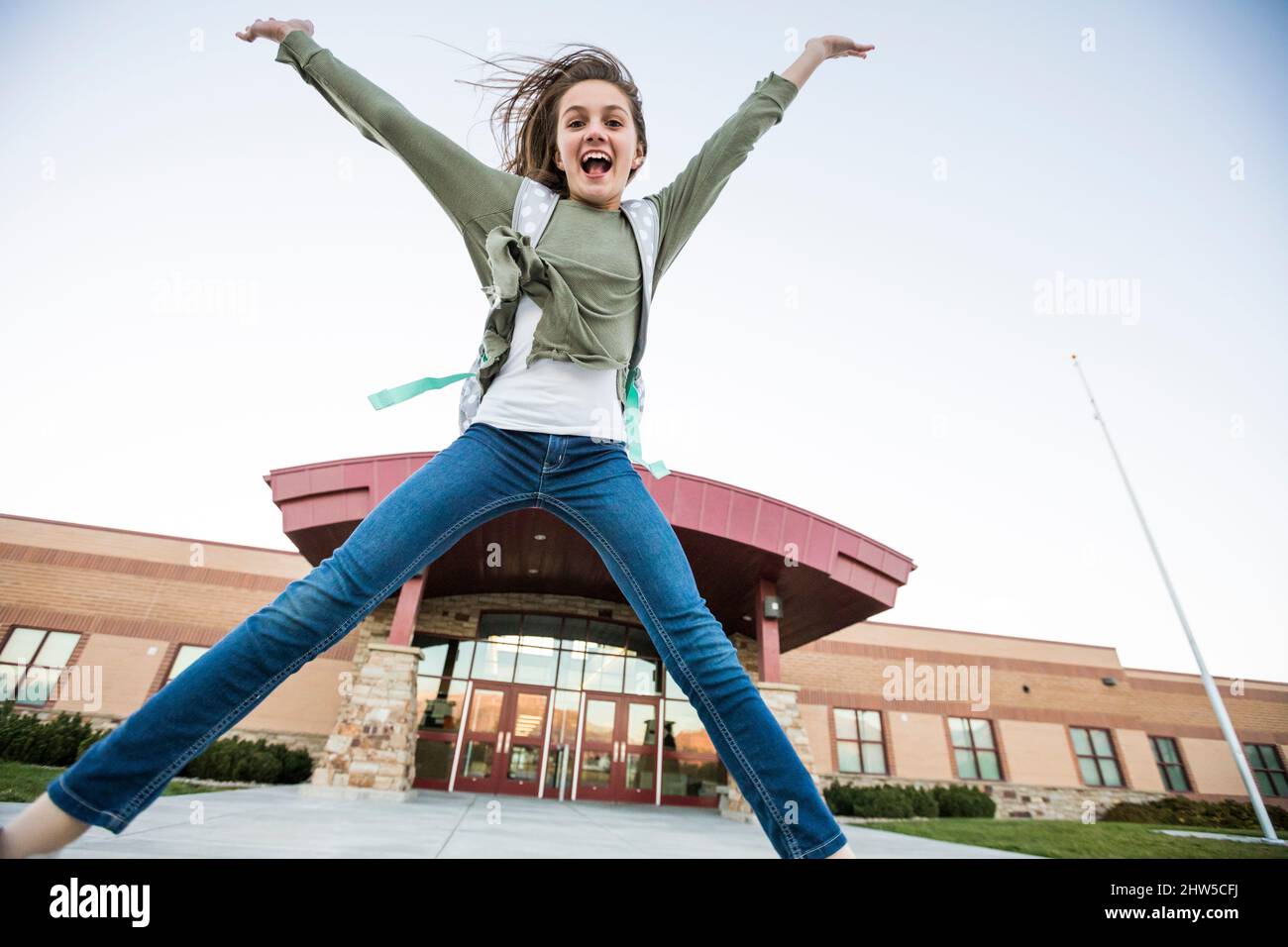 Stati Uniti, Utah, Lehi, ragazza sorridente (12-13) che salta di fronte all'edificio scolastico Foto Stock