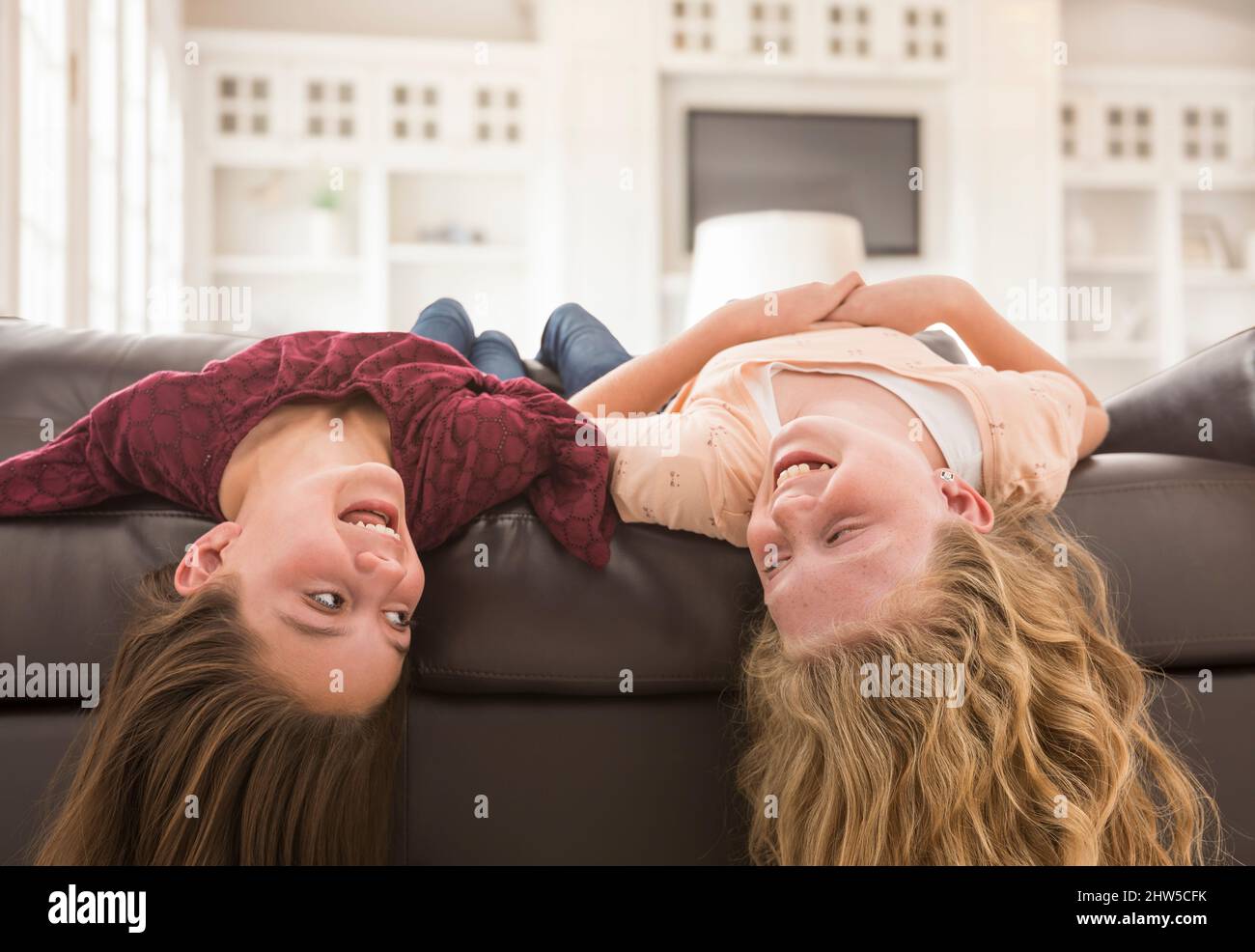 Sorelle (10-11, 12-13) che ridono sul divano Foto Stock