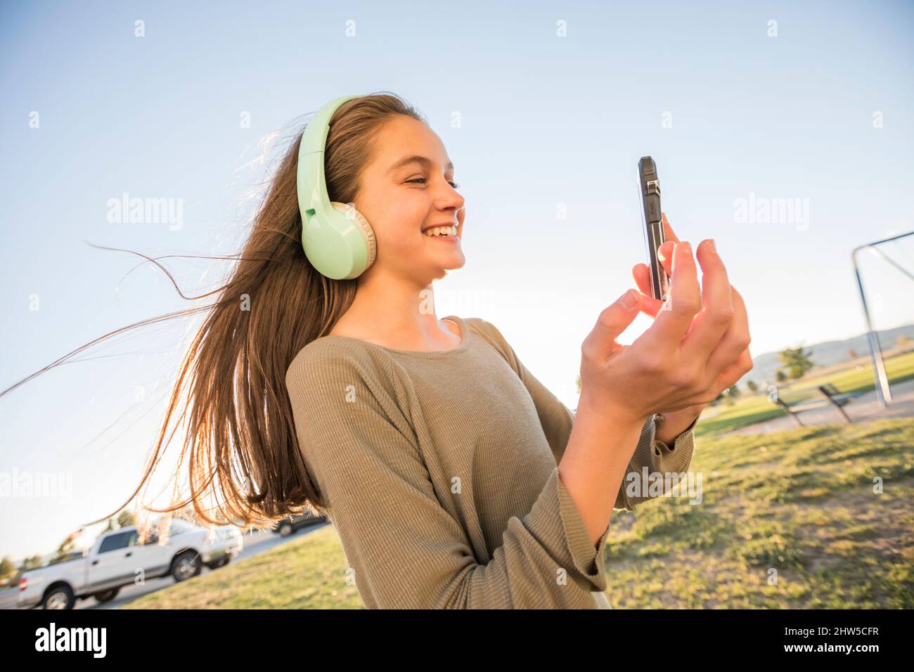 Ragazza sorridente (12-13) con cuffie e smartphone nel parco Foto Stock
