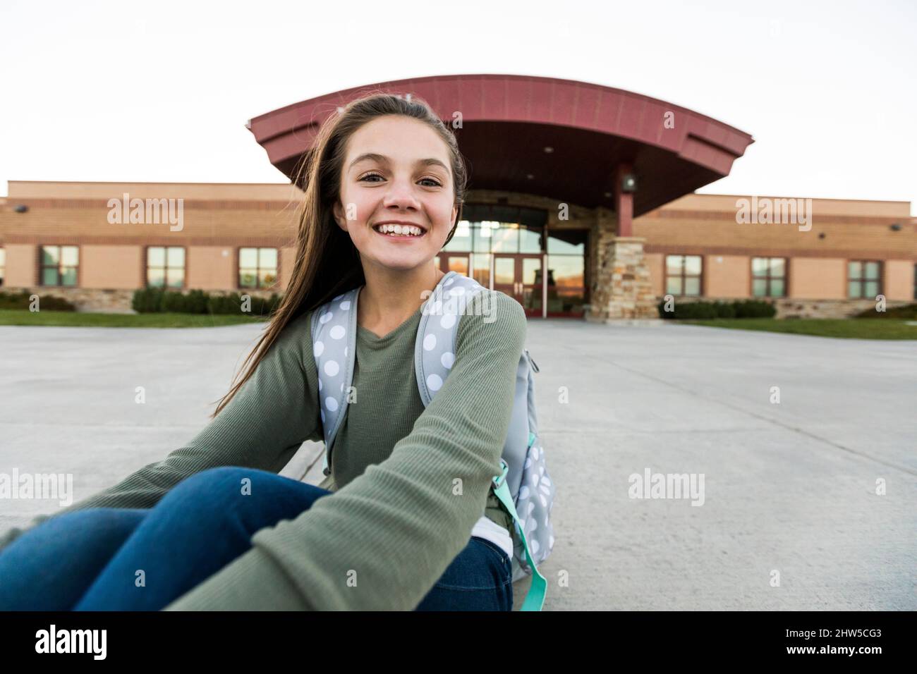 Stati Uniti, Utah, Lehi, Ritratto della ragazza sorridente (12-13) seduta davanti all'edificio scolastico Foto Stock