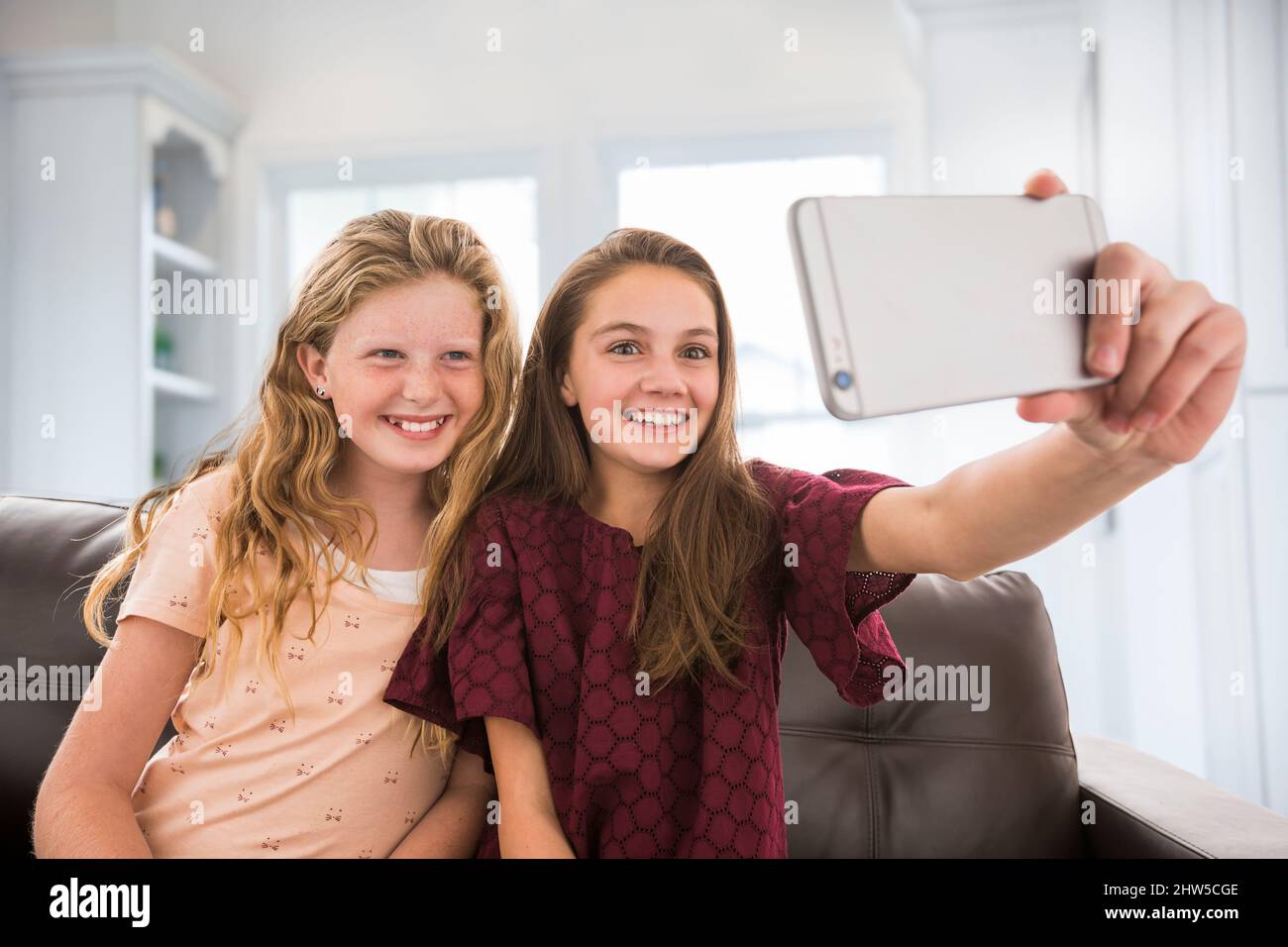 Sorridenti sorelle (10-11, 12-13) che prendono selfie a casa Foto Stock