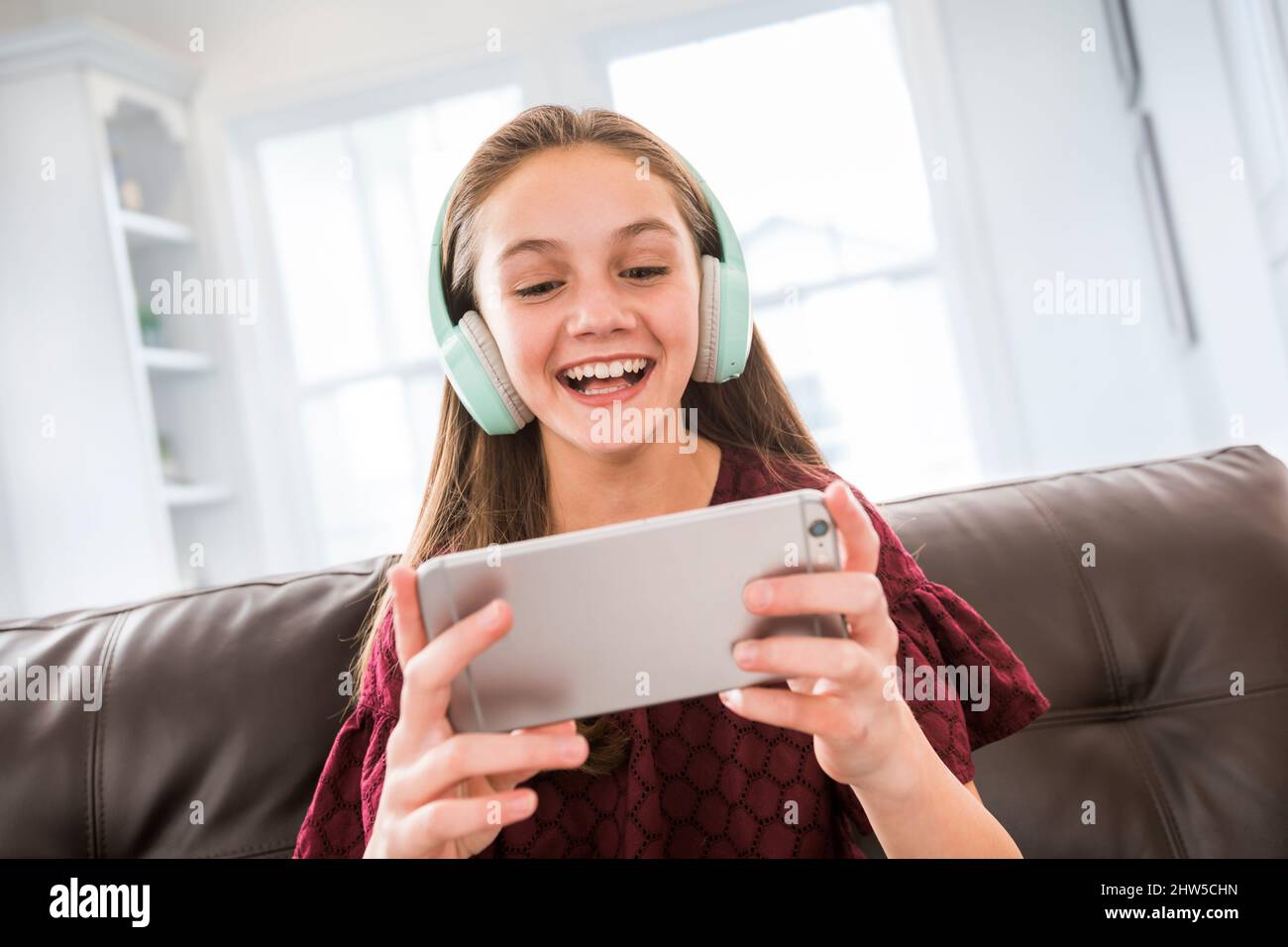 Ragazza sorridente (12-13) con cuffie e smartphone sul divano Foto Stock