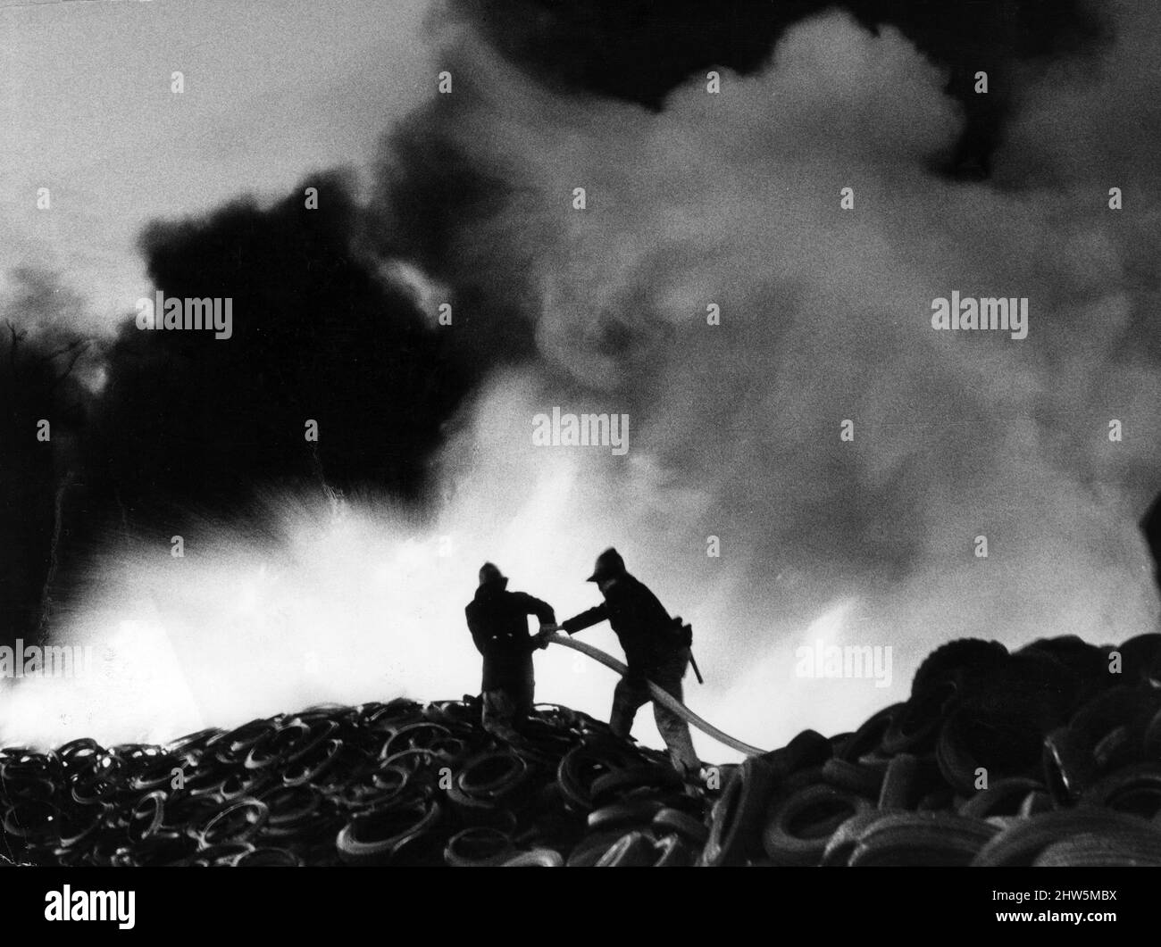 Incendio presso Tire Disposals Ltd, Thornliebank Industrial Estate, Glasgow, aprile 1968. Due vigili del fuoco si ergono su un tumulo di 25 piedi di gomma brilla ... e fumo nero bilici in tutta la città. Foto Stock