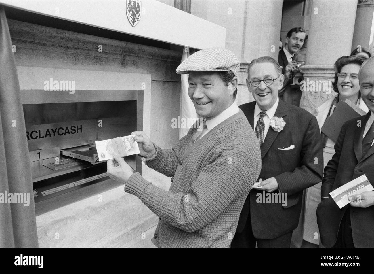 The Worlds First ATM, Cash Machine viene presentato alla Barclays Bank, a Enfield, Middlesex, appena a nord di Londra. 27th giugno 1967. L'immagine mostra l'attore Reg Varney nel suo cappuccio bianco. Barclays ATM, 27th giugno 1967. Sir Thomas Bland, vice presidente della Barclays Bank, rivela una cassa robot che eroga denaro in qualsiasi momento del giorno o della notte. Progettata e sviluppata in collaborazione con De la rue Instruments e con il Dipartimento dei servizi di gestione delle banche, la macchina BarclayCash è installata presso la filiale Enfield. Reg Varney, attore, ha preso il tempo dalle riprese per la serie televisiva "Beggar Your Neighbor" a Northwood To Foto Stock