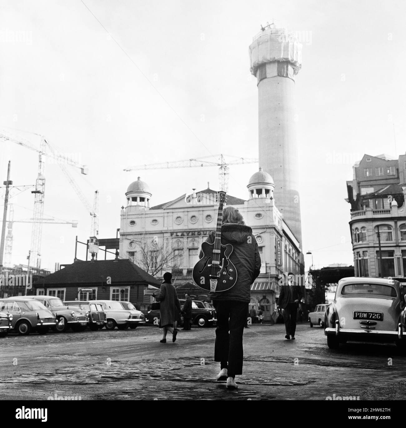 Una persona che cammina per le strade di Liverpool, portando una chitarra sulla schiena. Sullo sfondo è la radio City Tower, in costruzione. Liverpool, Merseyside. Circa 1967. Foto Stock
