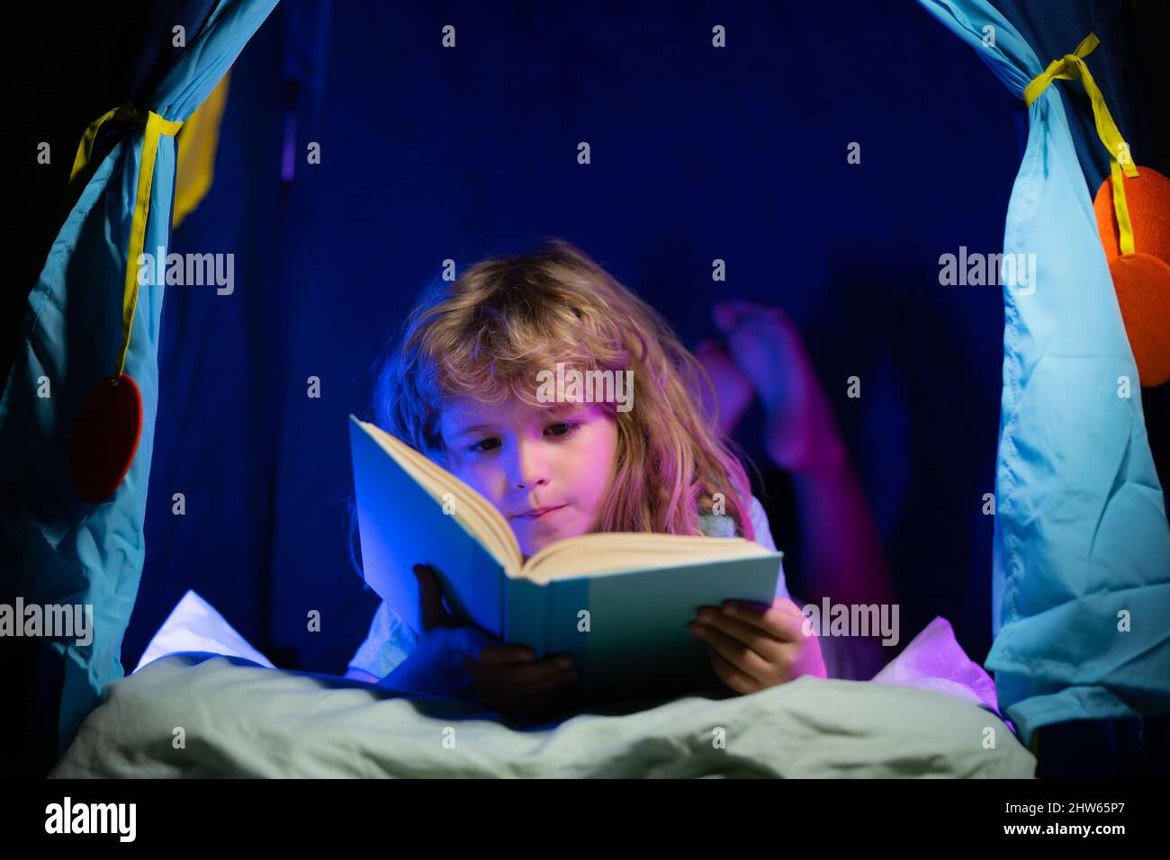 I bambini che leggono un libro nella casa oscura. Bambino ragazzo che legge  un libro sdraiato sul letto. I bambini hanno la faccia con la luce notturna.  Concetto di educazione e lettura.