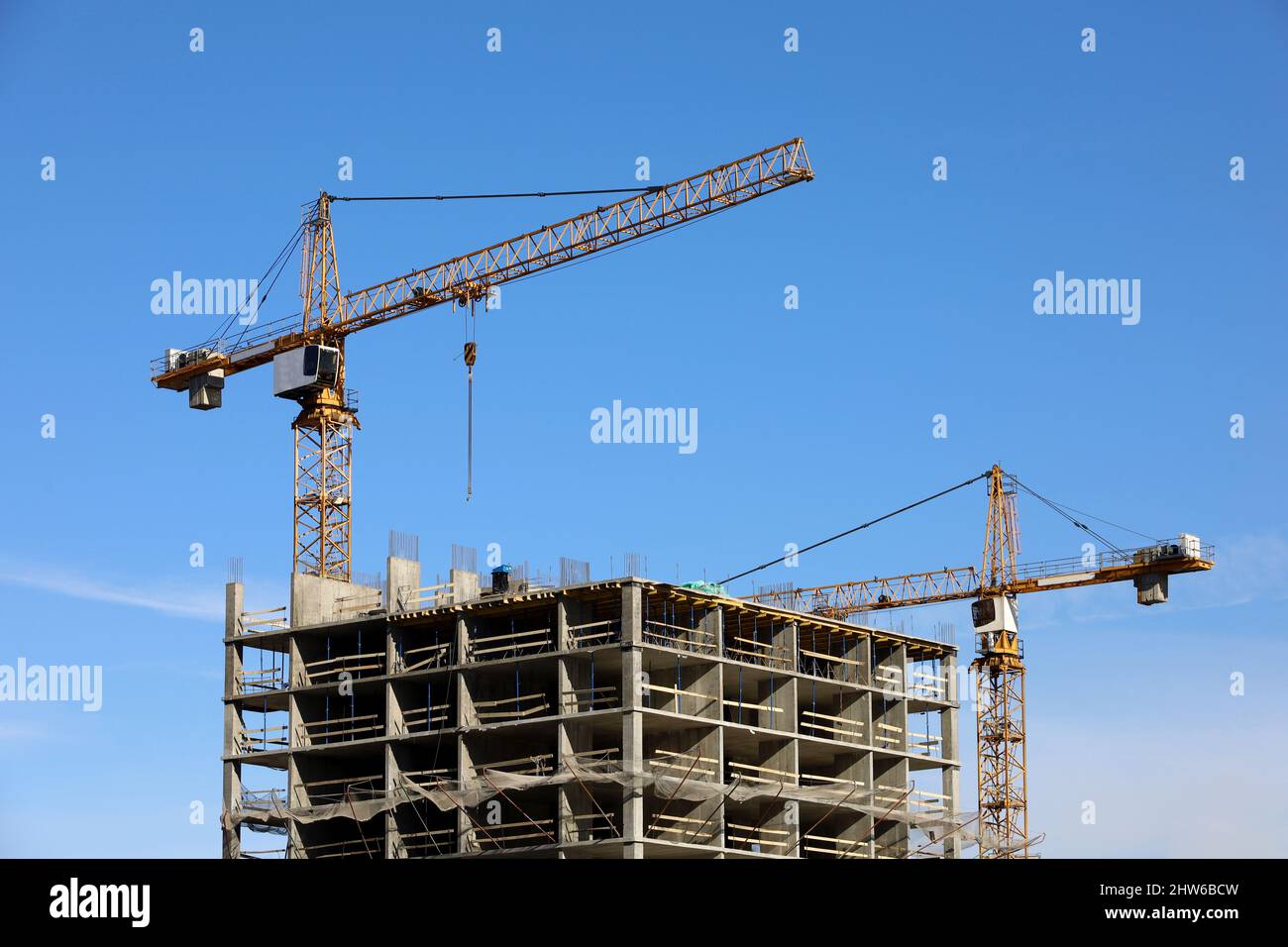 Costruzione torre gru sopra edificio residenziale incompiuto su sfondo cielo blu. Edilizia abitativa, condominio Foto Stock