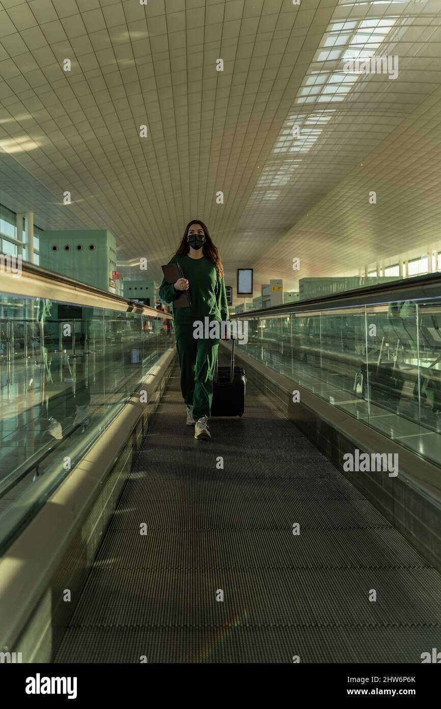 La donna spagnola cammina lungo il nastro trasportatore dell'aeroporto con il suo computer portatile e la valigia Foto Stock