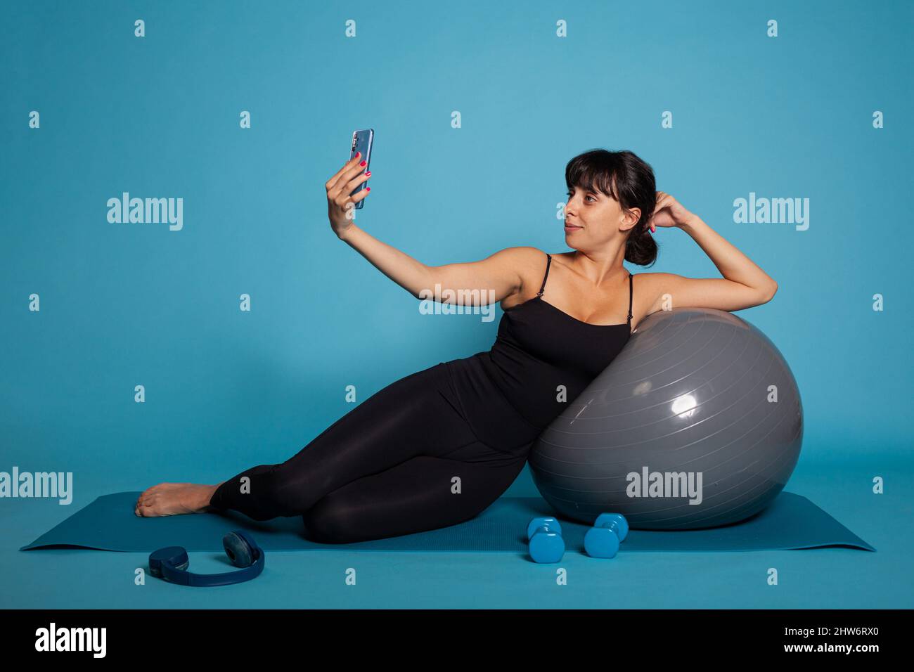 Donna atleta che si appoggia al pallone da yoga scattando foto utilizzando lo smartphone che mette sui social media. Personal trainer praticare yoga esercizio allungare i muscoli del corpo lavorando a uno stile di vita sano Foto Stock