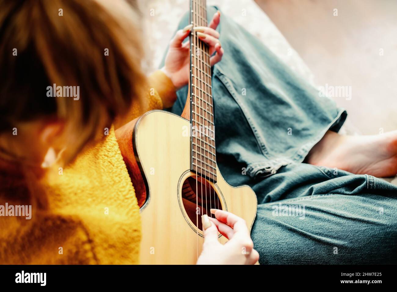 Giovane ragazza con unghie lunghe suona la chitarra acustica a casa.  L'adolescente si siede sul divano in camera e impara a suonare lo strumento  musicale. Sfondo. Primo piano Foto stock - Alamy
