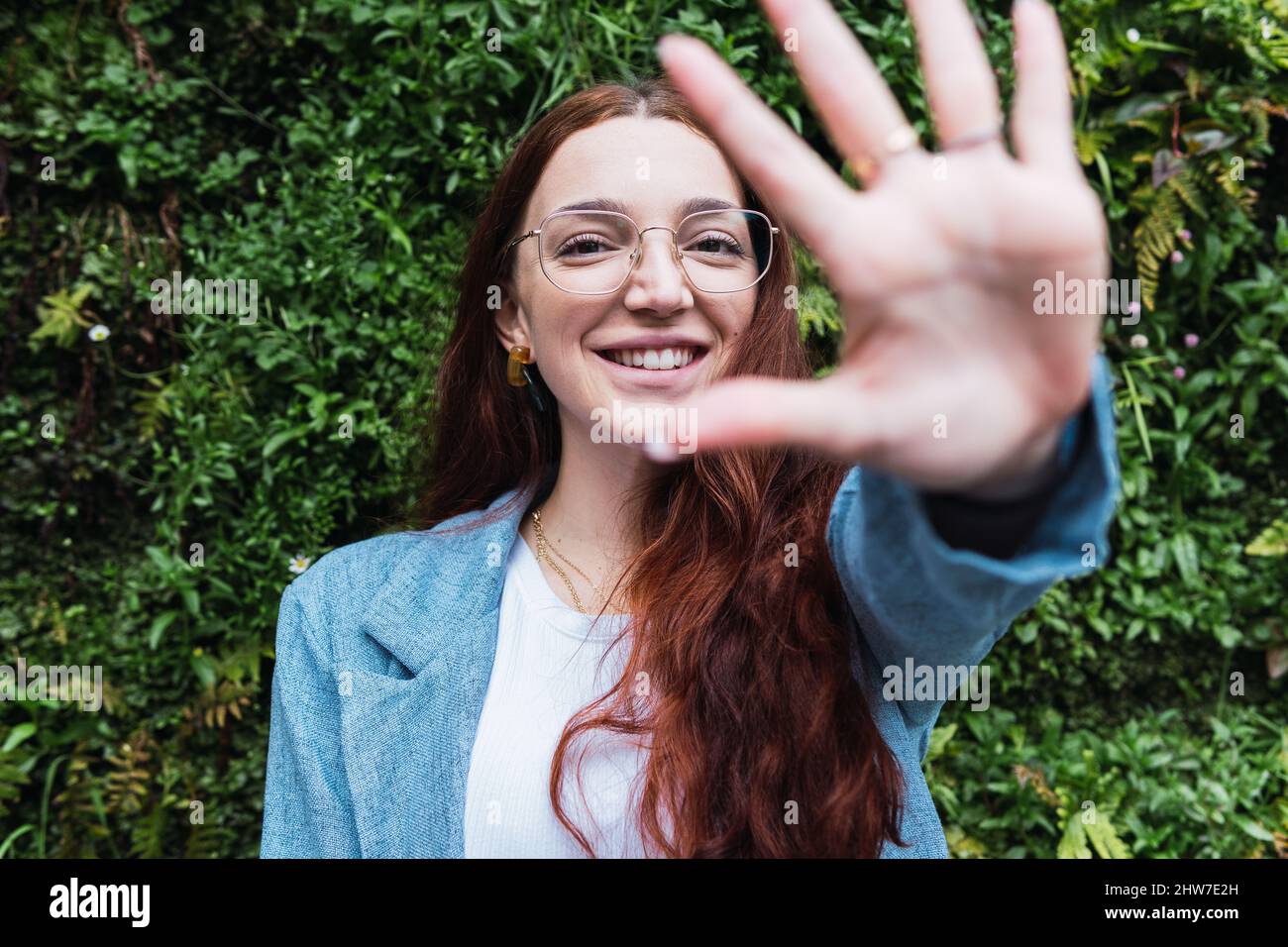 Ritratto di donna sorridente con lunghi capelli rossi che tirano la mano verso la fotocamera. Ritratto di bellezza di donna naturale divertirsi Foto Stock