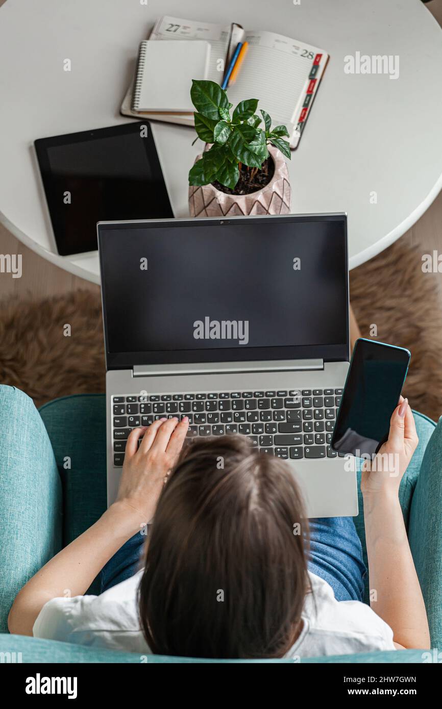 Giovane donna che usa un notebook per lavorare a casa, lavorare in remoto, più dispositivi Foto Stock