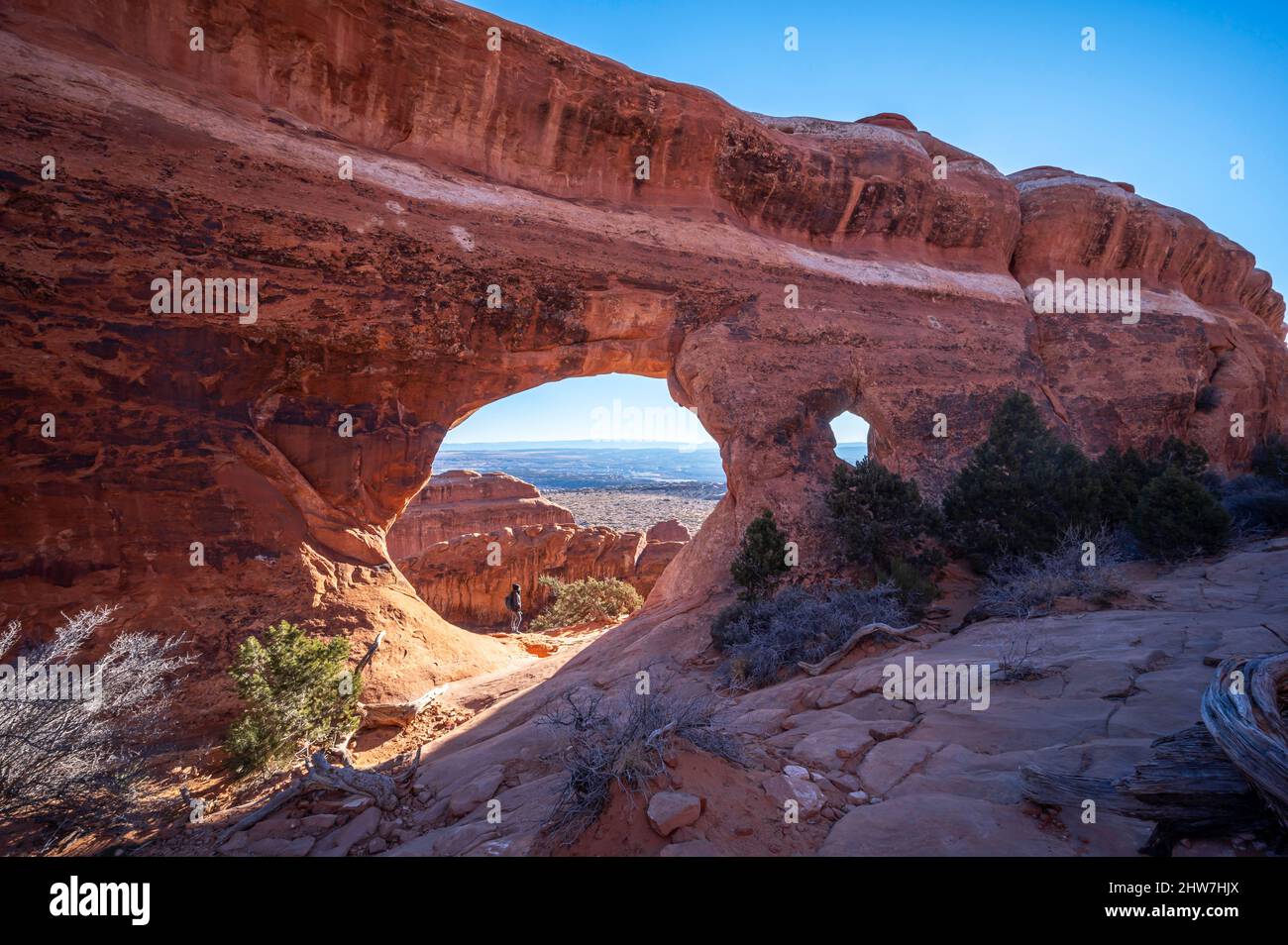 Escursionista in piedi sotto il Partition Arch nel Parco Nazionale Arches Foto Stock