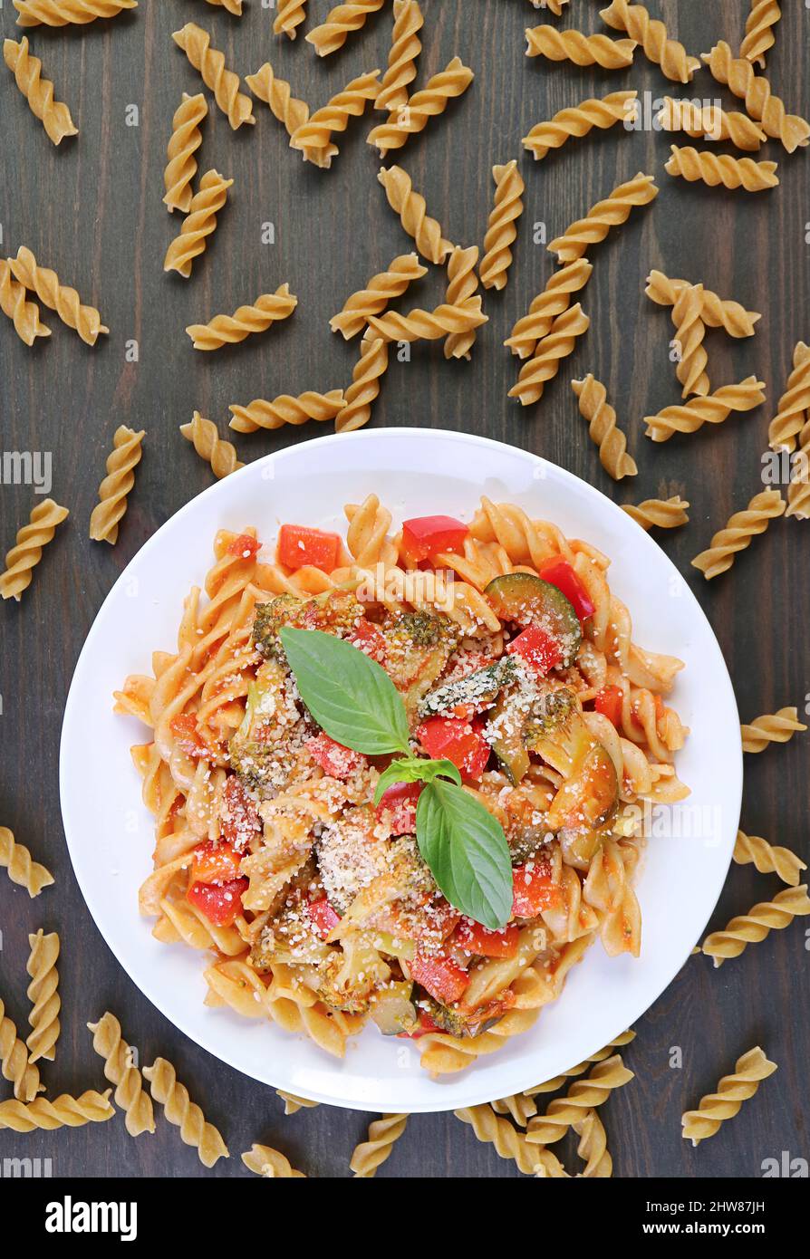 Piatto di succulenta pasta di Fusilli di frumento intero in salsa di pomodoro con pasta secca sparsa intorno Foto Stock