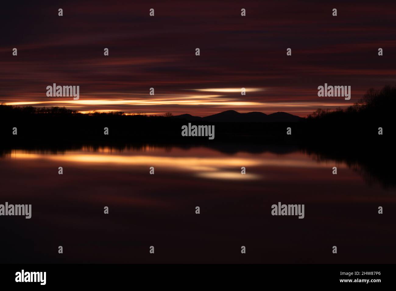 Paesaggio rurale al crepuscolo con luce sbiadente a lunga esposizione - astratta nube scura su silhouette di montagna e riflesso simmetrico in acqua di fiume Foto Stock