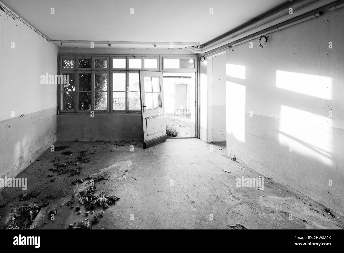Vecchia casa abbandonata. La stanza è distrutta, le pareti sono rotte, spazzatura sul pavimento, caos. Messa a fuoco selettiva. Bianco e nero. Foto Stock