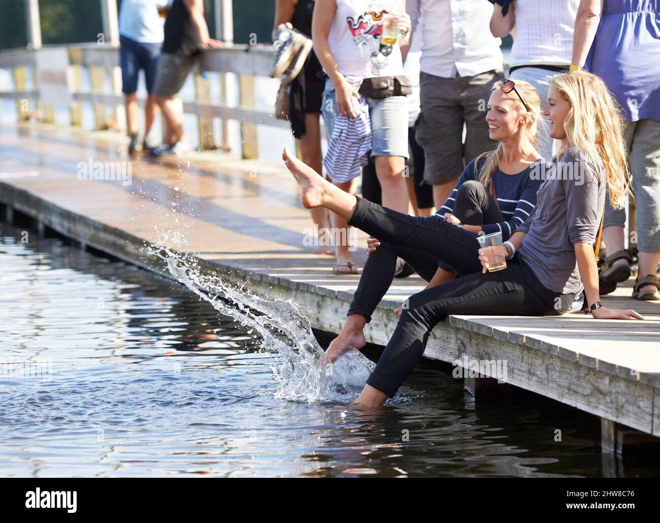 Dare ai loro piedi un meritato riposo. Scatto di due giovani donne seduti con i piedi in acqua in un festival all'aperto. Foto Stock