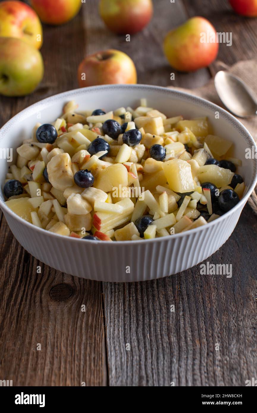 Macedonia di frutta in una ciotola su tavola di legno. Immagine verticale con spazio di copia Foto Stock