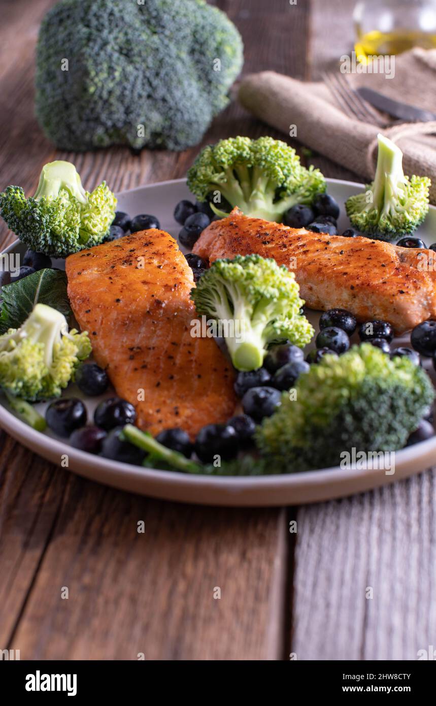 Cibi sani su un piatto come salmone, broccoli e mirtilli freschi. Servito su un tavolo rustico e in legno. Immagine verticale Foto Stock