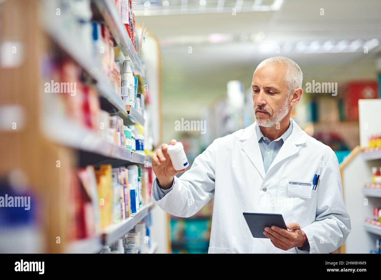 Questo non appartiene qui.... Scatto corto di un bel farmacista maschio maturo usando una compressa mentre lavora in farmacia. Foto Stock