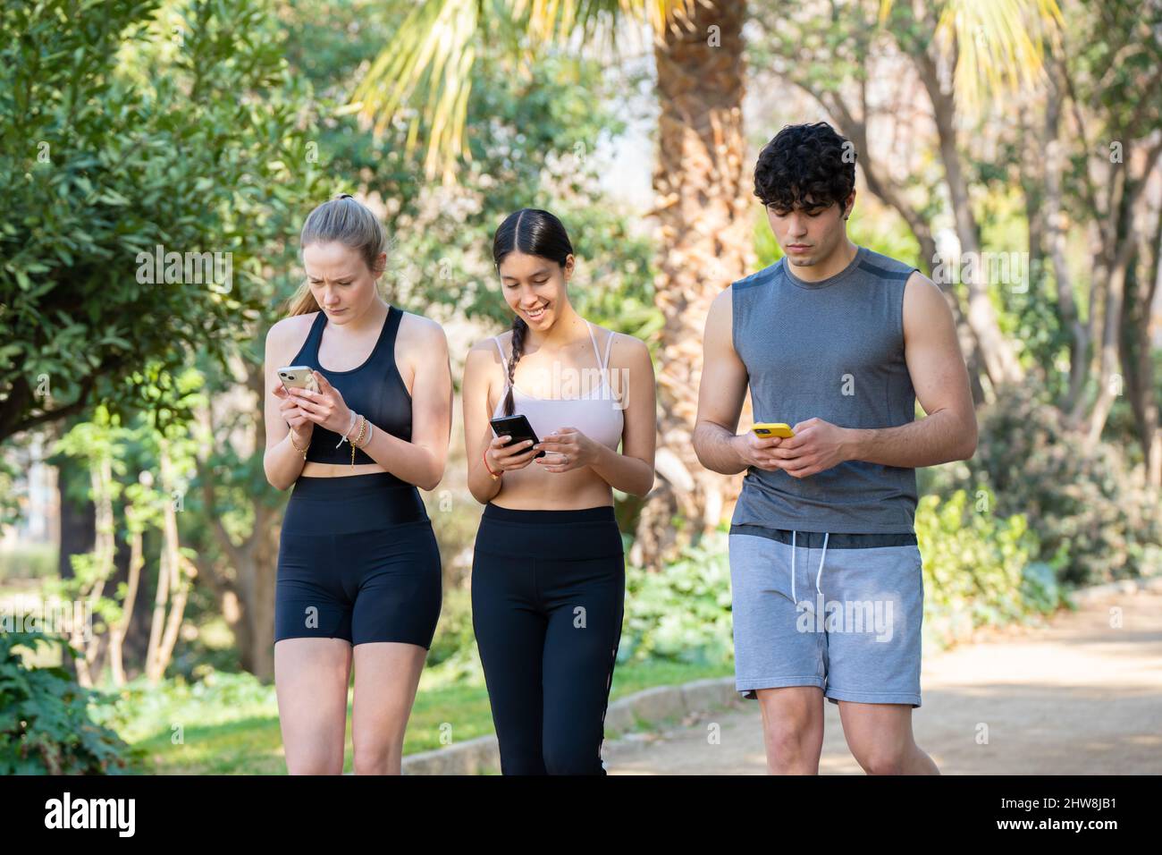 Tre giovani atleti stanno camminando concentrati sul loro telefono nel parco Foto Stock
