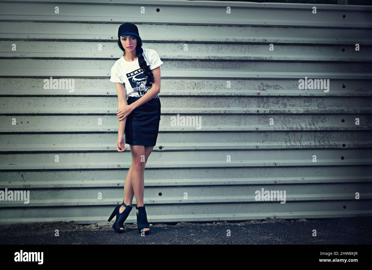 Urban chic. Ritratto di una giovane donna vestita con eleganza in piedi davanti ad un muro di metallo. Foto Stock