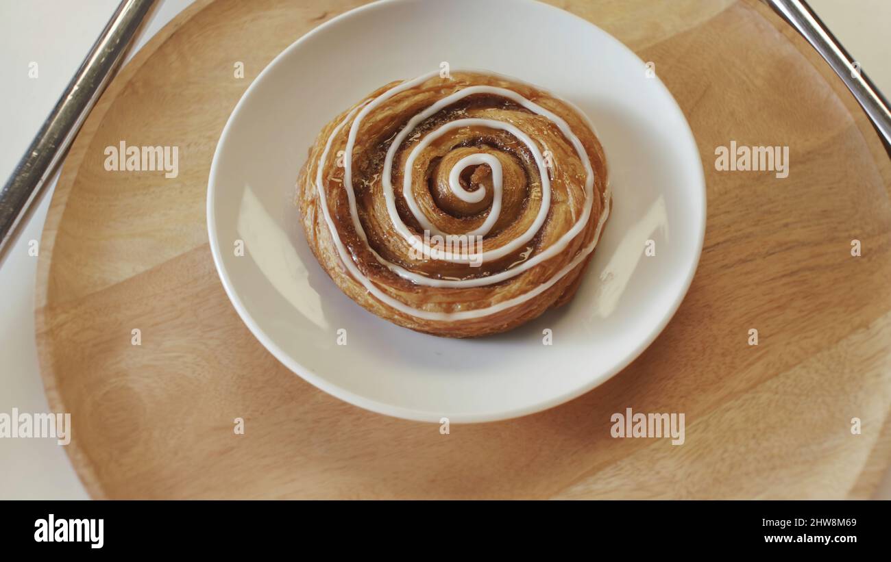Concetto di panetteria e pasticceria. Gustosi panini dolci con miele e smalto bianco adagiati sul piatto bianco e girevoli sul pannello rotondo in legno. Foto Stock