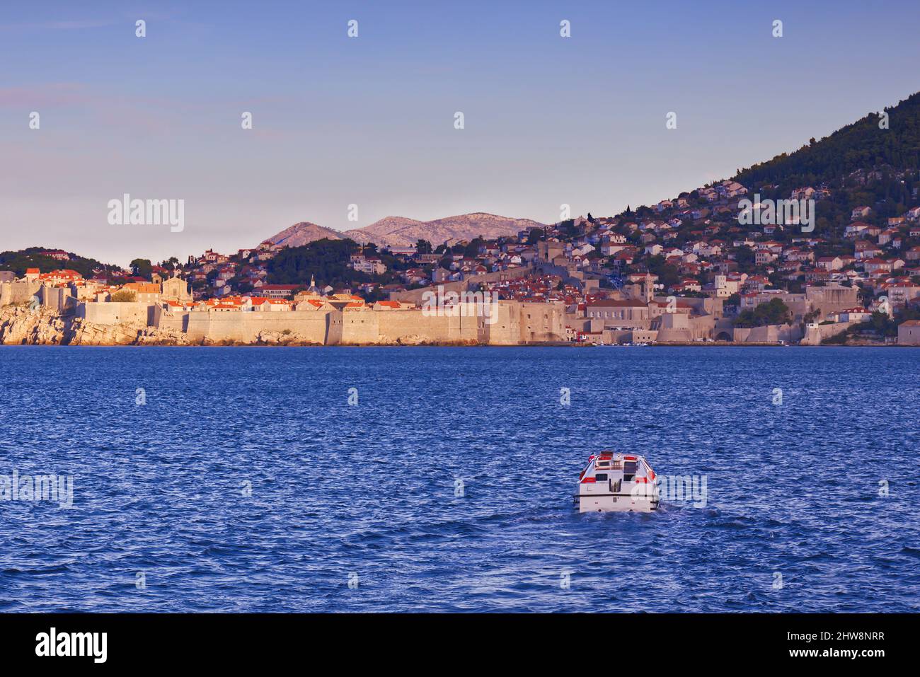 Dubrovnik, Croazia - arrivando via mare - una piccola barca si avvicina alla città, con le mura della città e montagne lontane in vista Foto Stock