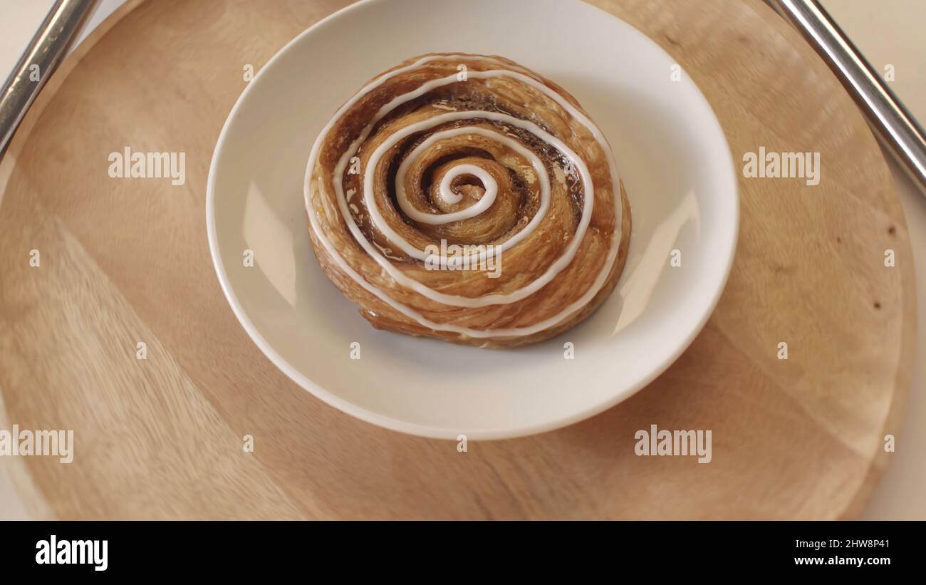 Concetto di panetteria e pasticceria. Gustosi panini dolci con miele e smalto bianco adagiati sul piatto bianco e girevoli sul pannello rotondo in legno. Foto Stock