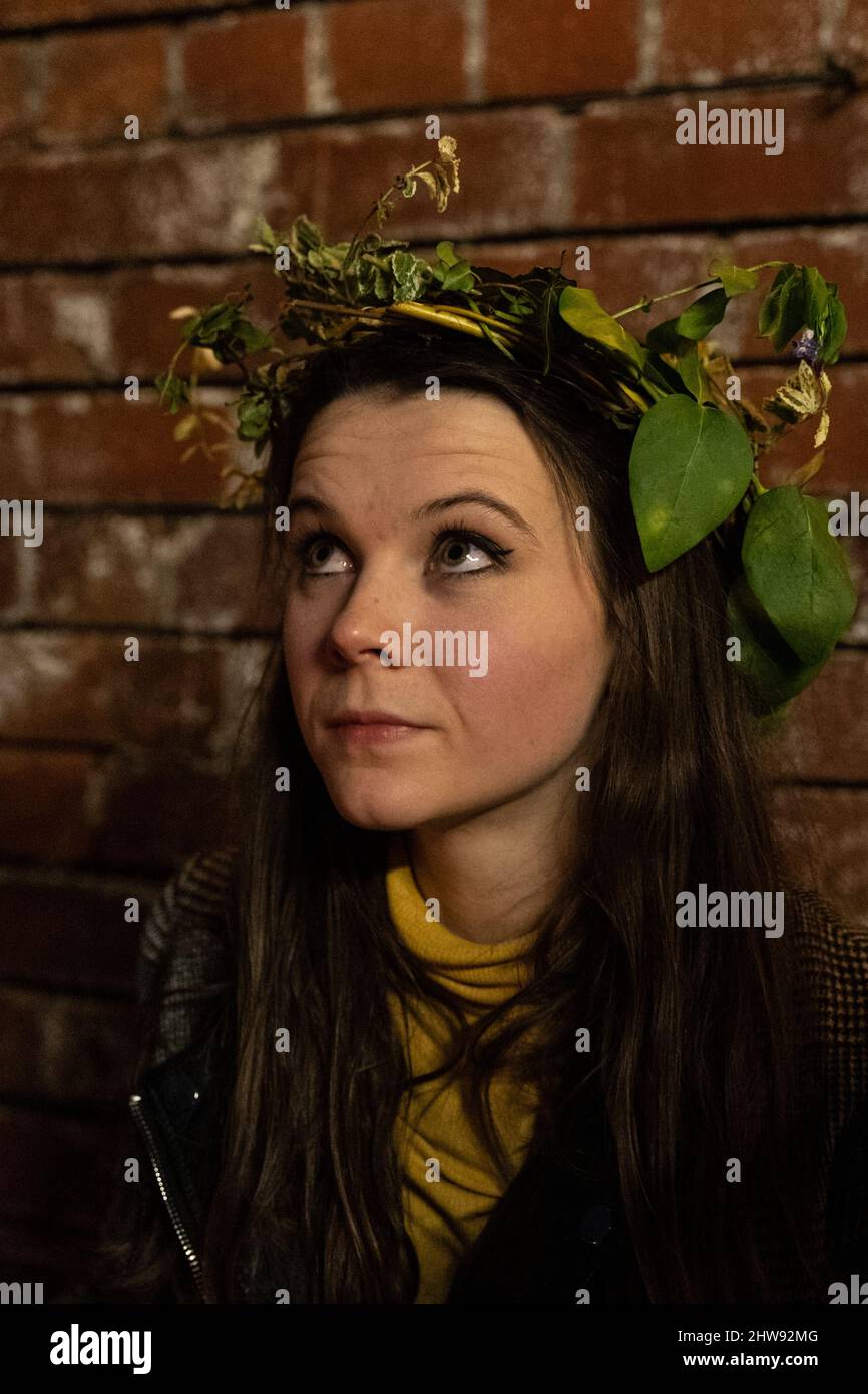 Giovane donna che indossa una corona in foglia verde naturale sullo sfondo della parete di mattoni Foto Stock