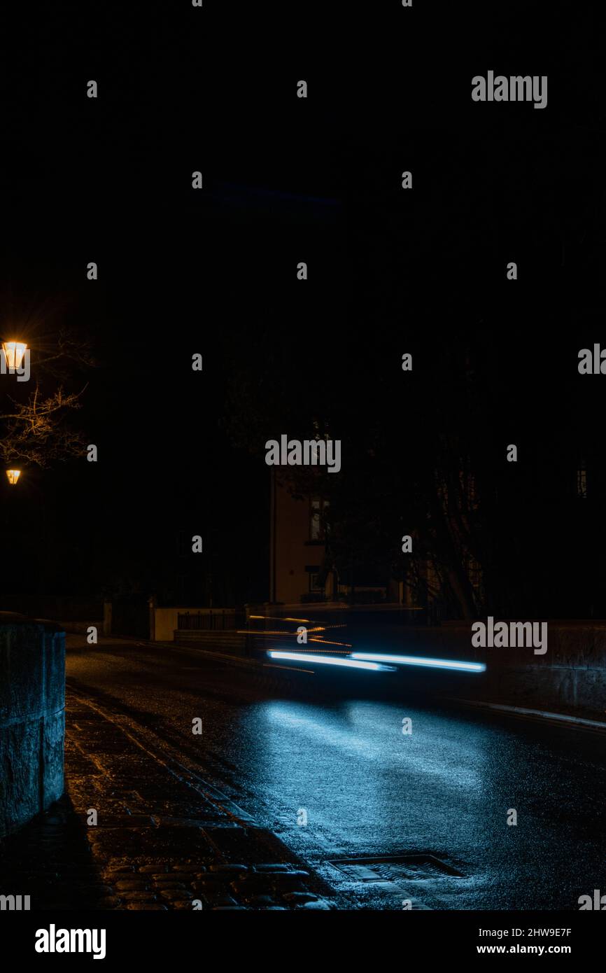 Una foto a lunga esposizione di un'auto in movimento lungo la strada principale di Prestbury, giocando con il contrasto del blu freddo dell'auto e la luce streetlamp. Foto Stock