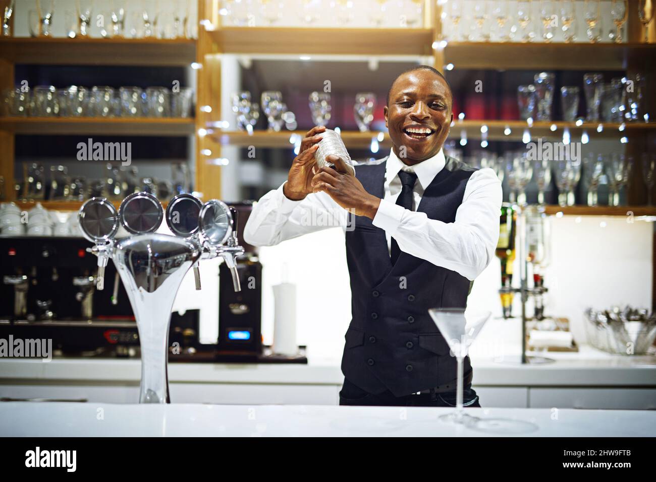 Il suo tempo di scuotere le cose in su dentro qui. Scatto corto di un barista ben vestito in piedi dietro il bancone. Foto Stock