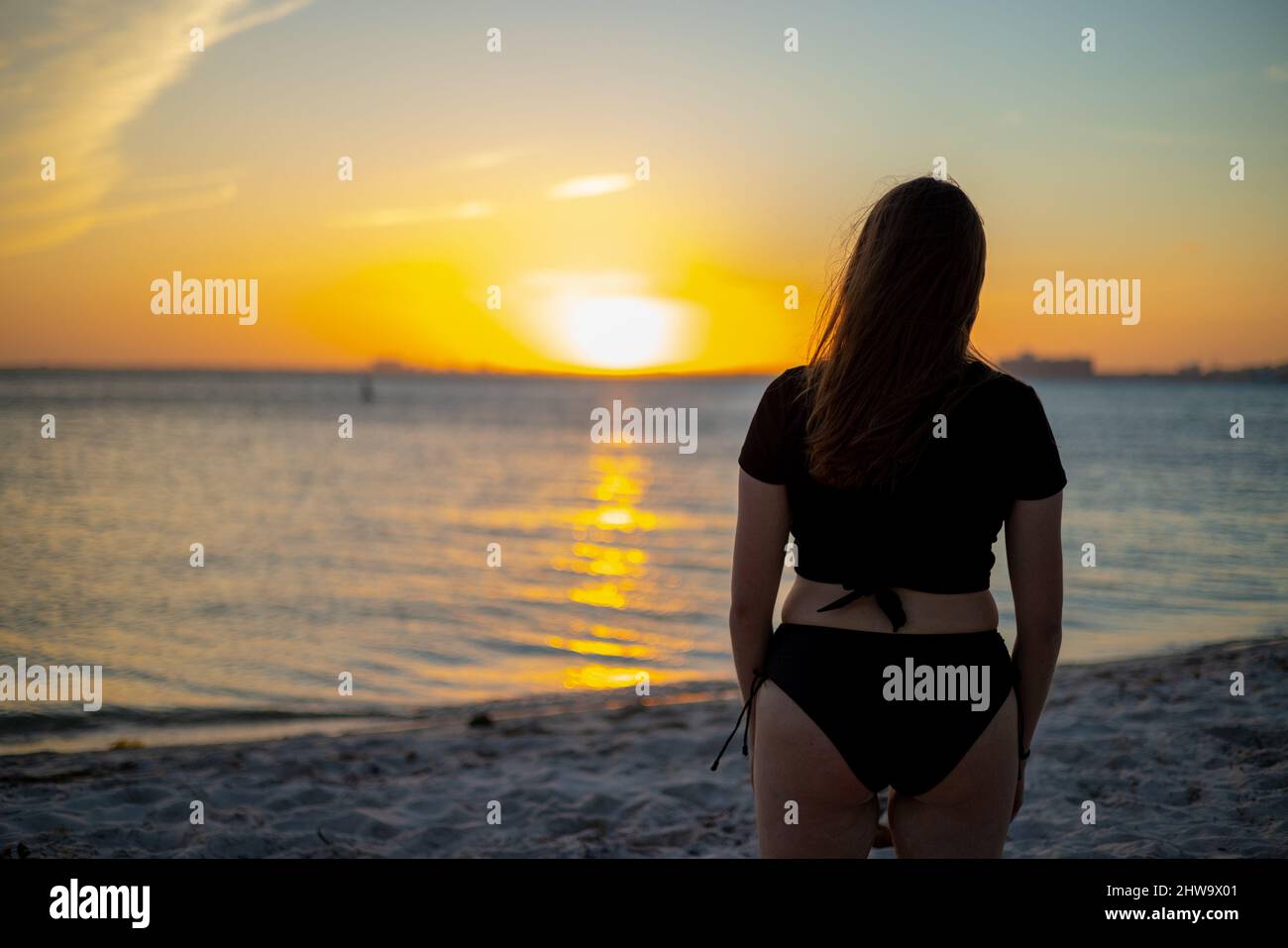 Giovane donna in costume da bagno in spiaggia guarda il tramonto Foto Stock