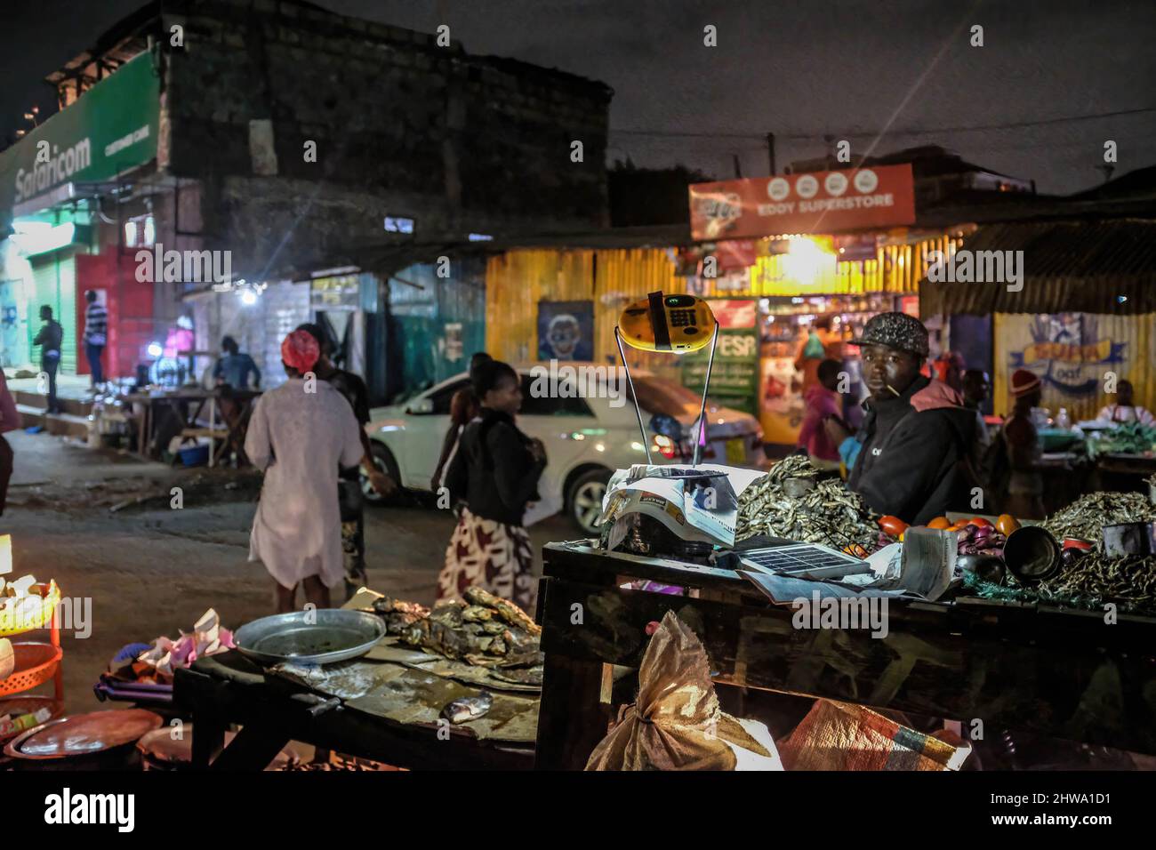 Un venditore di strada che usa una lampada solare mentre fornisce i servizi ai suoi clienti giù dalle strade in baraccopoli di Kibera.in baraccopoli di Kibera, la maggior parte dei residenti specialmente i fornitori di strada, scuole private, organizzazioni non governative, luci di strada, e tutte le scuole utilizzano il sistema di energia solare a basso costo, che è una fonte di energia più affidabile ed economica. Ciò ha reso più facile il riciclaggio della maggior parte dell'energia elettrica consumata dai residenti e ha anche contribuito a ridurre l'elevato numero di morti che si verificano a causa delle scosse elettriche e degli incendi di slum quotidiani. Foto Stock