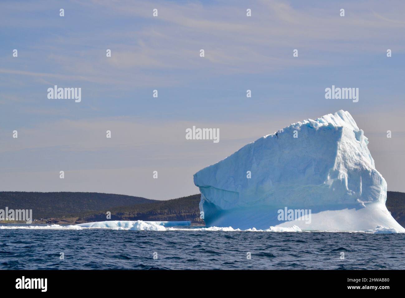 Metà soleggiato e ombreggiata iceberg nella baia fuori St. John's con la costa all'orizzonte durante la primavera Foto Stock