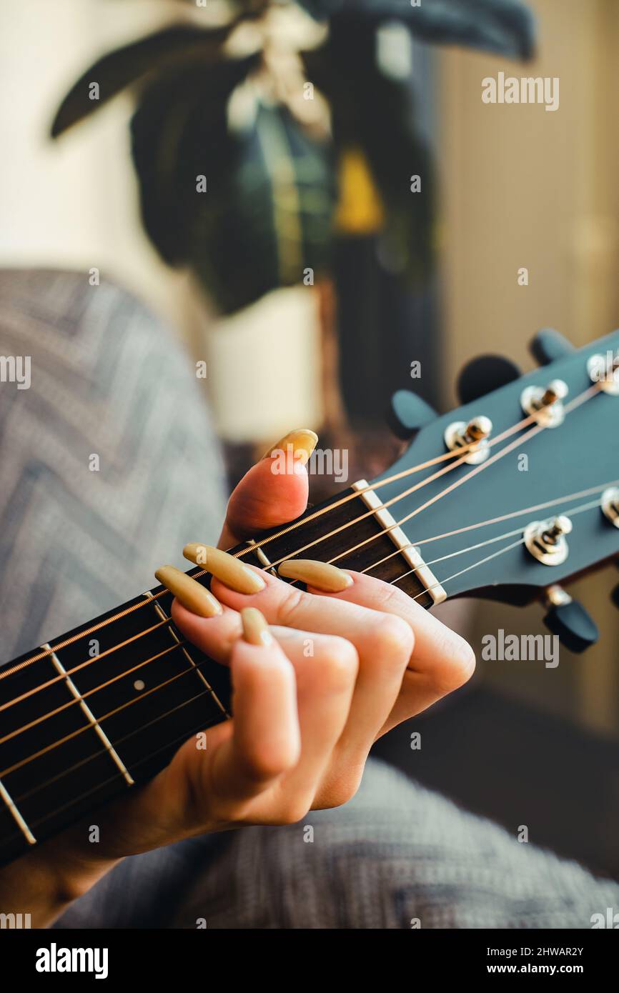 Ragazza suona la chitarra. La mano della donna con le unghie lunghe stringe  le corde sulla tastiera della chitarra. Primo piano Foto stock - Alamy