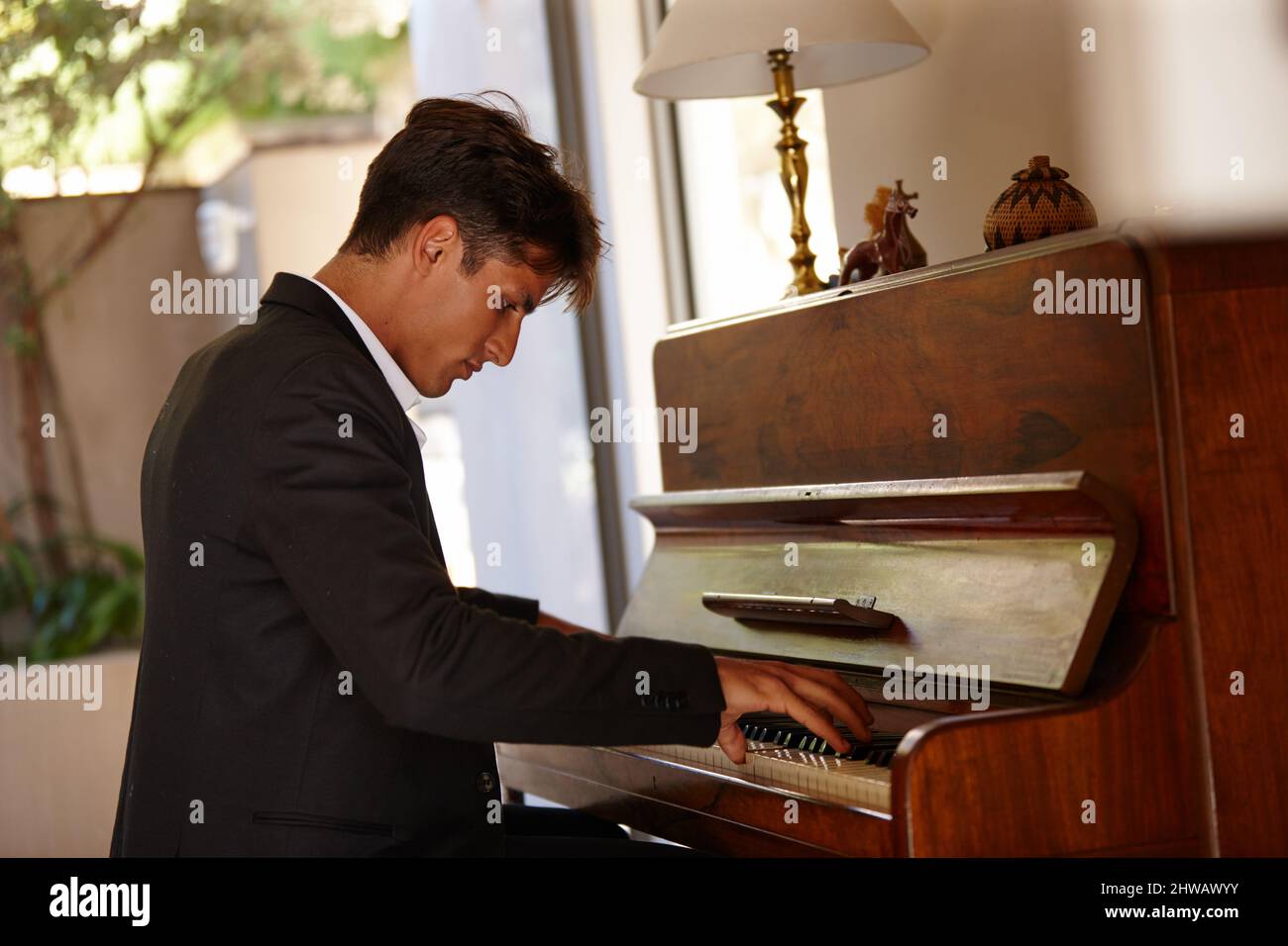 Perdendosi nella musica. Scatto di un bel giovane che suona il pianoforte a casa. Foto Stock