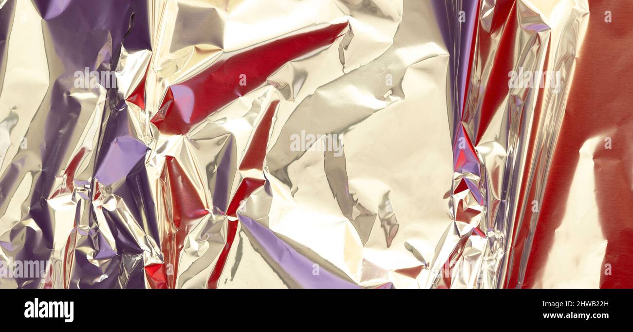 Astratto argento alluminio rugoso foglio multicolore sfondo texture riflette luce rossa e viola. Lucentezza metallizzata in lamina argentata Foto Stock