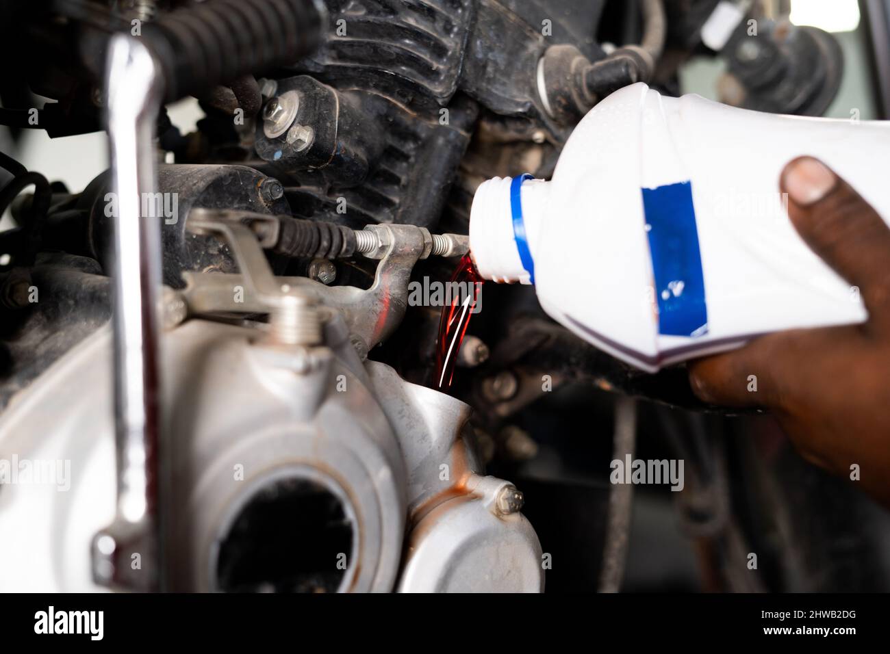 Primo piano delle mani del meccanico che versano olio nel motore in officina - concetto di manutenzione motobike e lubrificazione del motore. Foto Stock