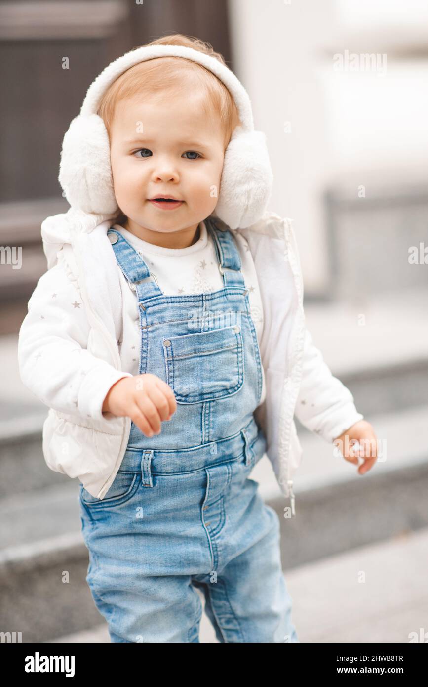 Ragazza sorridente carina 1-2 anni indossare pantaloni casual denim e top bianco in città strada all'aperto. Guardando la fotocamera. Infanzia. Primavera. Foto Stock