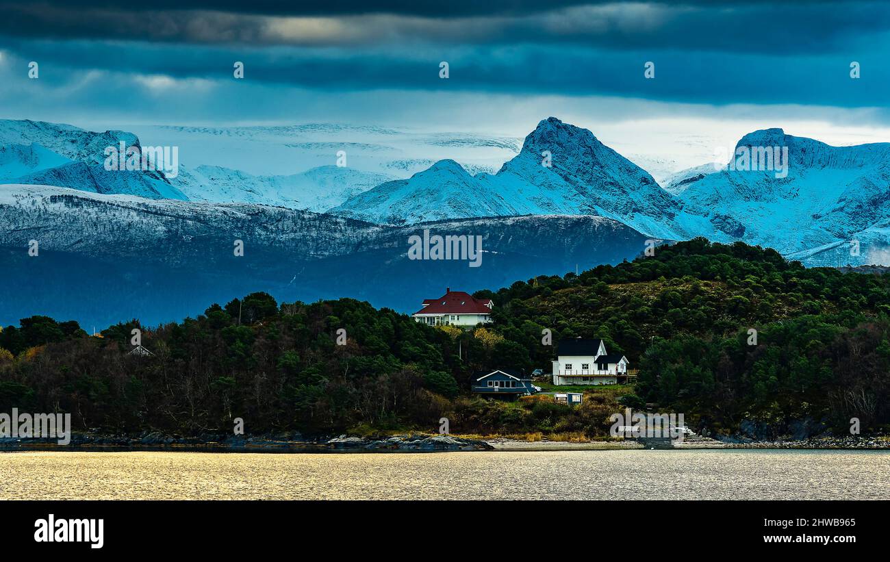 kleines Dorf an der norwegischen Küste in der Gegend von tons, mit schneebedeckten Bergen im Hintergrund und Schwartisen Gletscher, in Wolken gehüllt. Foto Stock